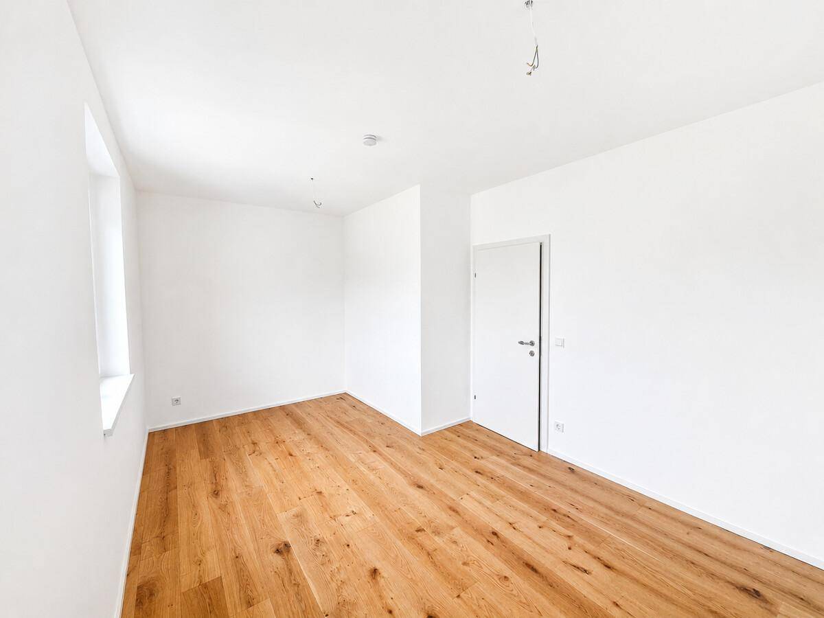 Helles, unmöbliertes Zimmer mit Eichenparkett und einem Fenster für viel Tageslicht.