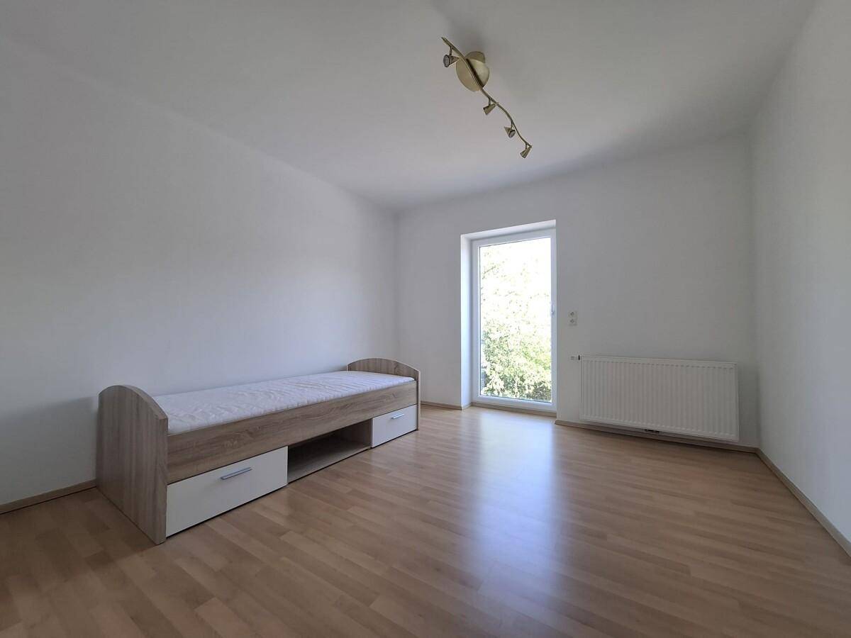 Helles Schlafzimmer mit Holzbett, Parkettboden und Zugang zum Außenbereich.
