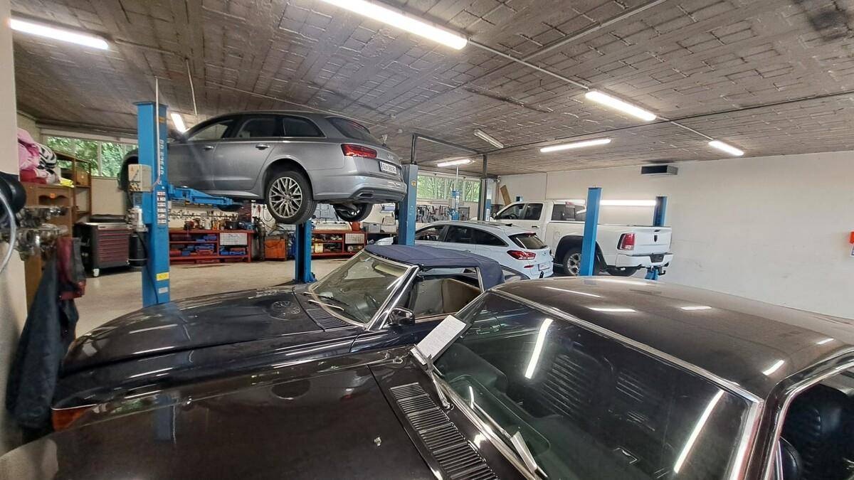 Werkstattbereich mit mehreren Fahrzeugen auf Hebebühnen und klassischen Autos, unter einer Beton-Decke.