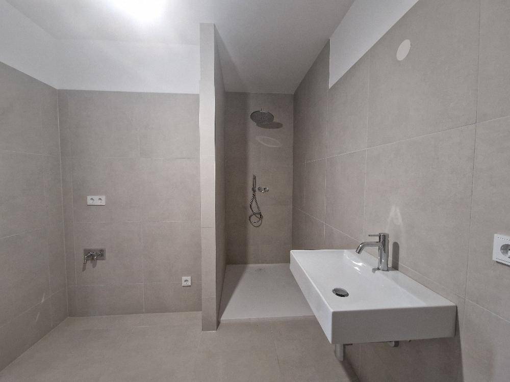Modernes Badezimmer mit wandmontiertem Waschbecken und begehbarer Dusche, in neutralen Farben.