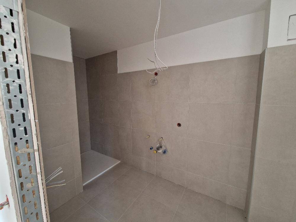 Badezimmer im Rohbau mit grauen Fliesen an Wänden und Boden, vorbereitet für die Installation.