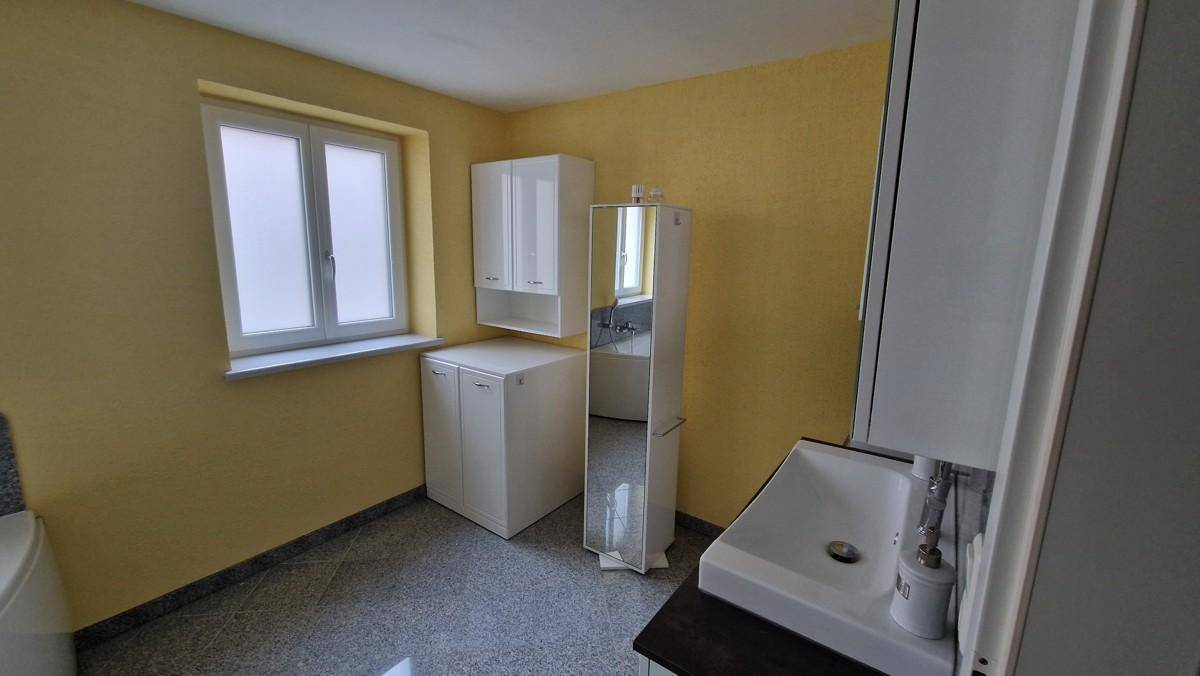 Badezimmer mit Fenster, Waschbecken und weißen Schränken vor gelben Wänden, hell und funktional.