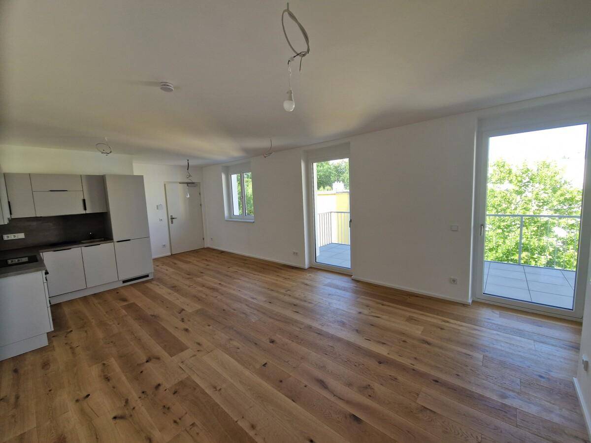 Lichtdurchfluteter Wohnbereich mit Zugang zum Balkon und integrierter Küchenzeile.