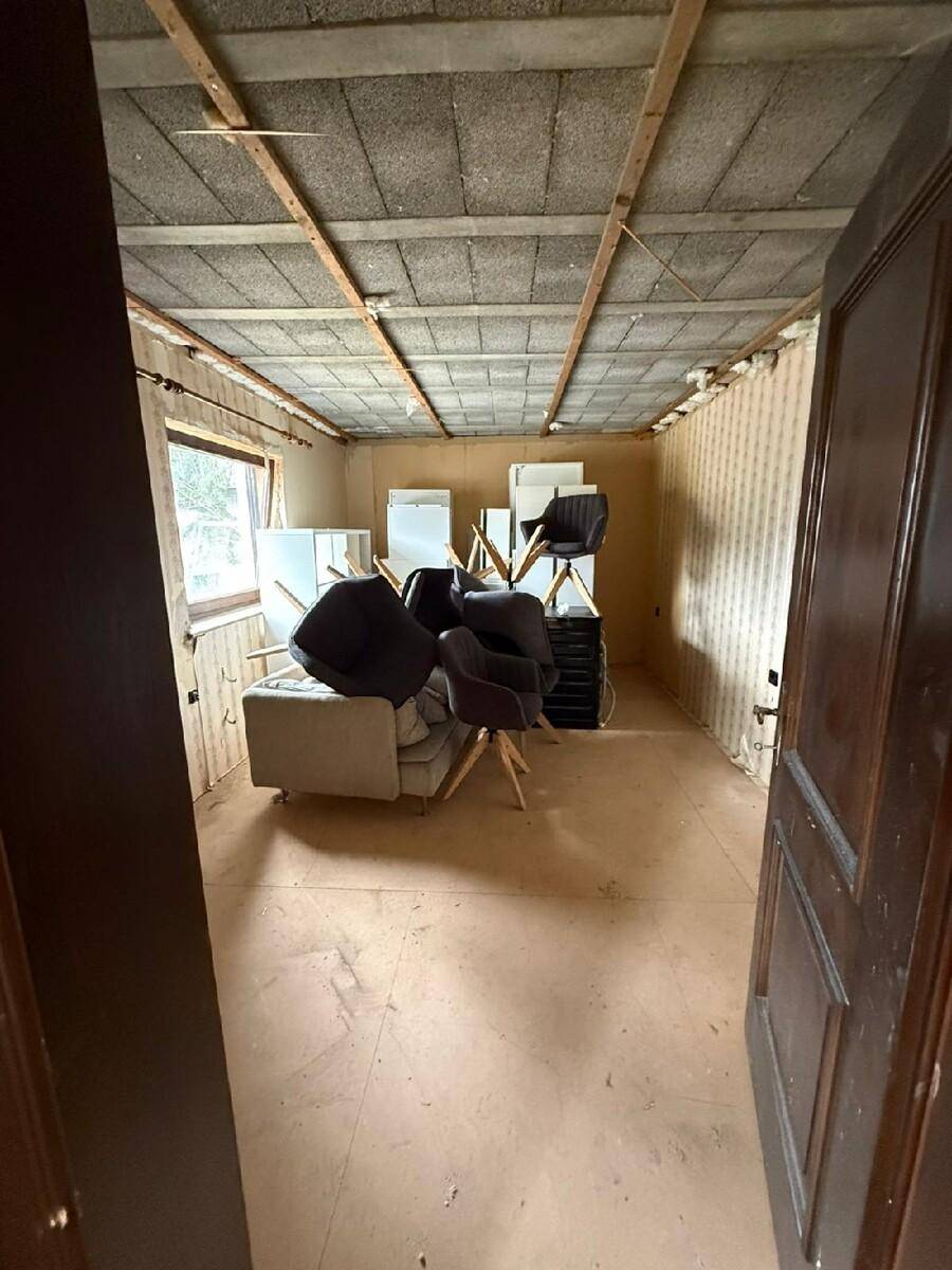 Raum im Rohbauzustand mit sichtbarer Deckenkonstruktion und gelagerten Möbeln, in Renovierung.