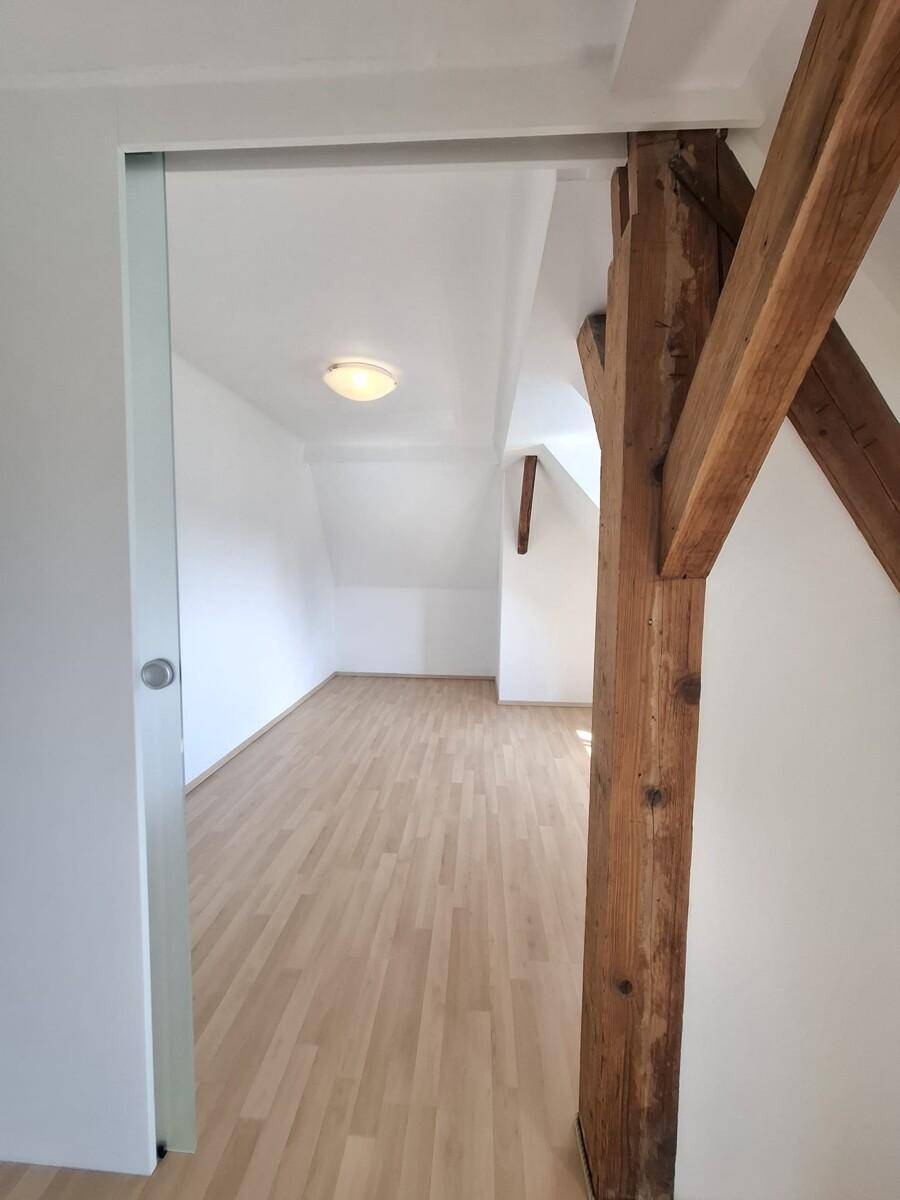 Dachgeschosszimmer mit sichtbaren Holzbalken, Parkettboden und viel Tageslicht.