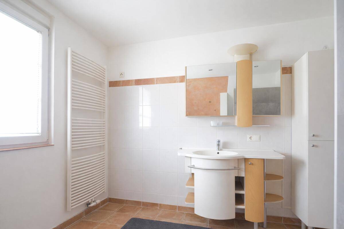 Helles Badezimmer mit Fenster, Einzelwaschbecken, beheiztem Handtuchhalter und Fliesenboden.