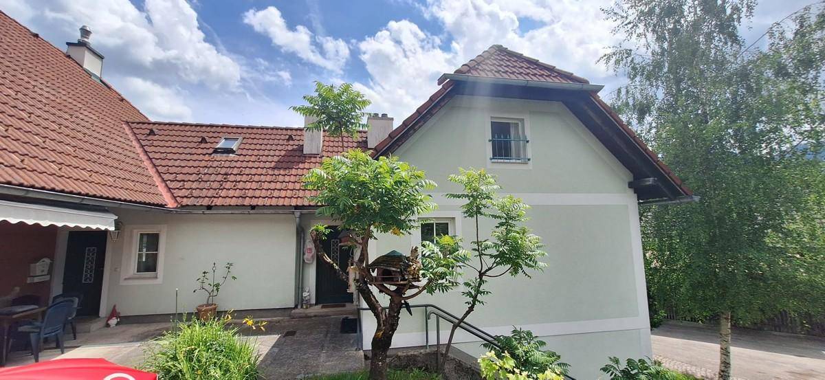 Seitenansicht des Hauses mit hell gestrichener Fassade, rotem Ziegeldach und einem kleinen Baum.