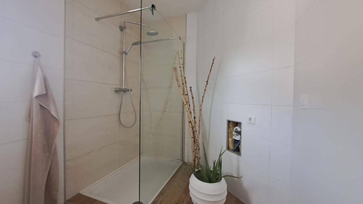 Ebenerdige Dusche mit Glasabtrennung und Holzoptik-Fliesen, minimalistisch gestaltet.