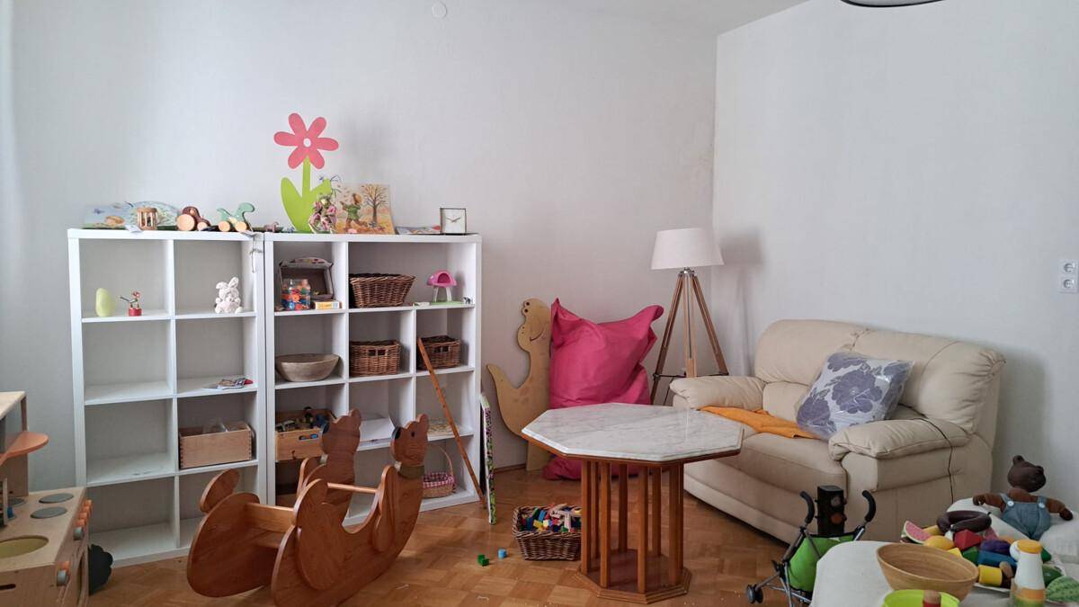 Gemütlicher Wohnbereich mit Kinderspielzeug, Regalen und einem kleinen Sofa.