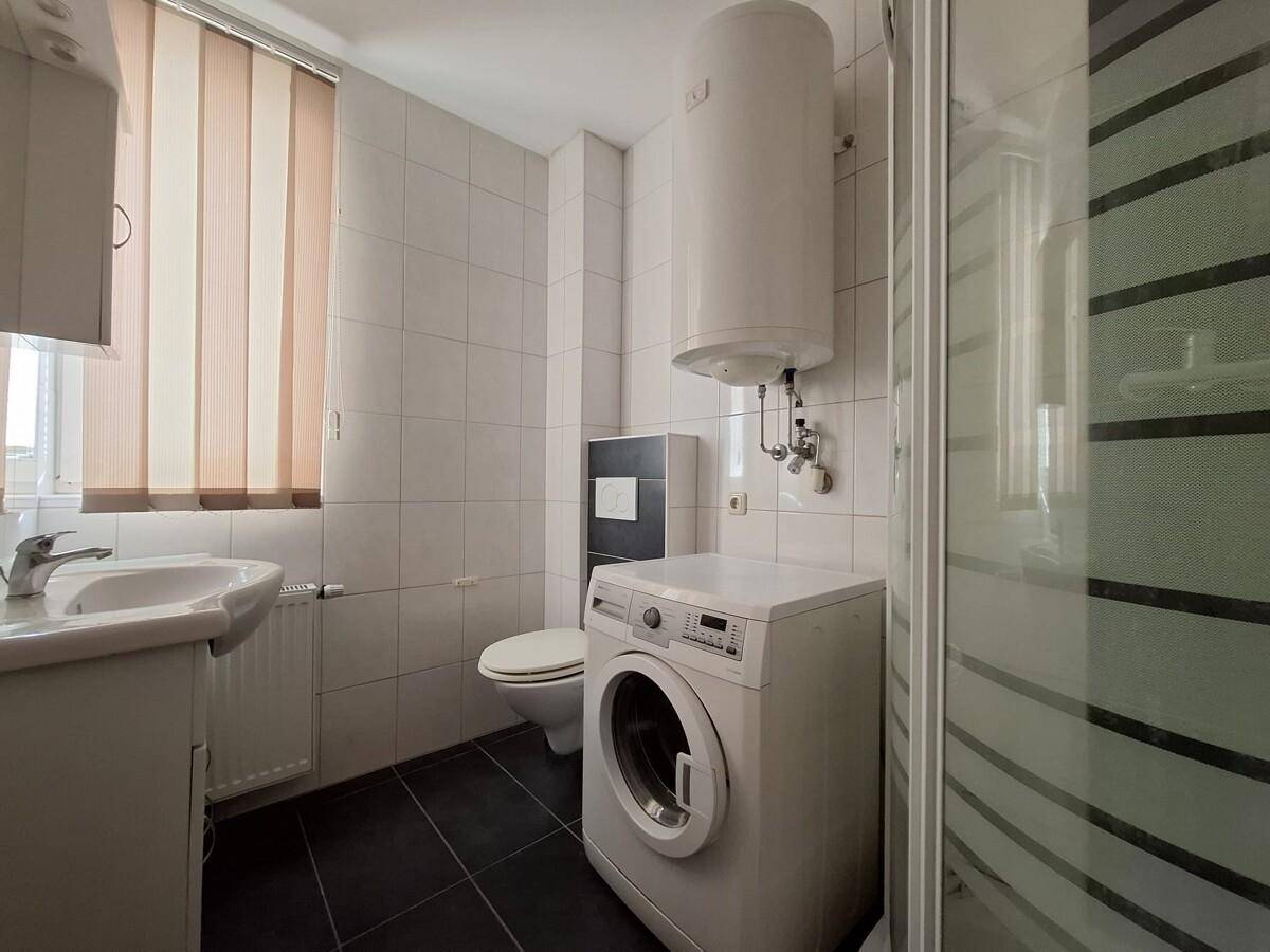 Badezimmer mit Dusche, WC, Waschmaschine und Boiler, gefliest in Weiß und Dunkelgrau.