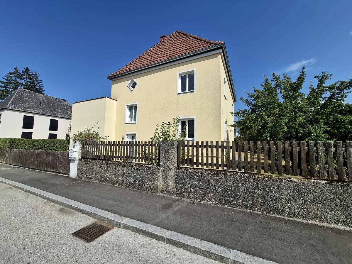 Vorderansicht des Hauses von der Straße aus mit Holzzaun und gepflegtem Garten.