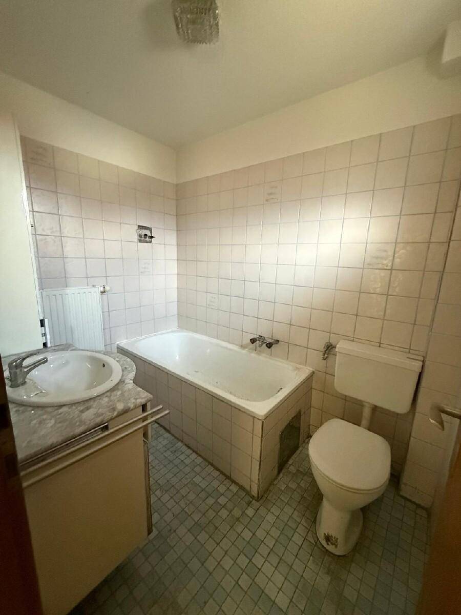 Badezimmer mit Badewanne, WC und Waschbecken, gefliest in hellen Pastelltönen im Stil der 80er Jahre.