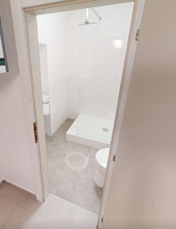 Helles Badezimmer mit ebenerdiger Dusche und modernem WC, durch eine Tür sichtbar.