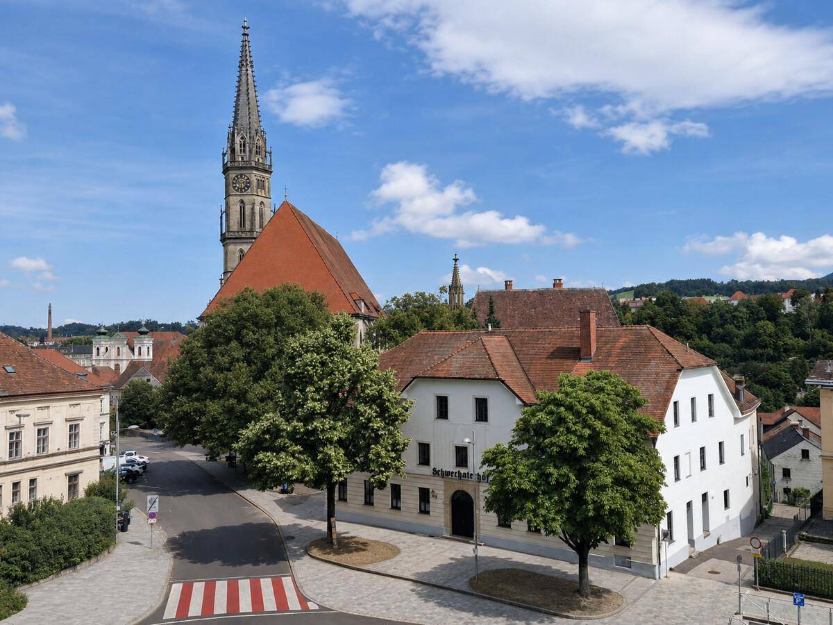 Panoramablick auf ein traditionelles Gebäude mit Kirchturm und die umliegende historische Stadtlandschaft unter blauem Himmel.