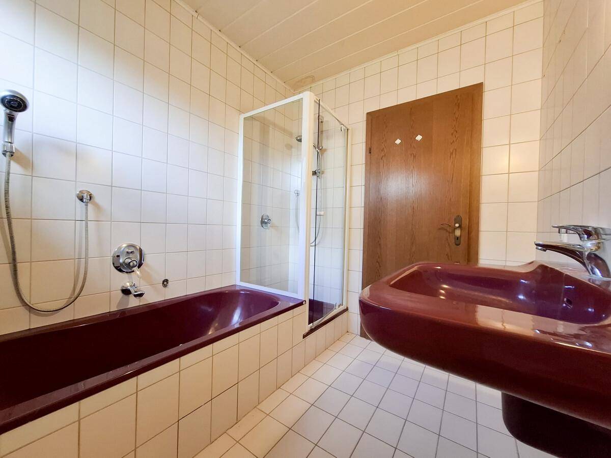Badezimmer mit Fliesen, Badewanne, Duschkabine und rotem Waschbecken.