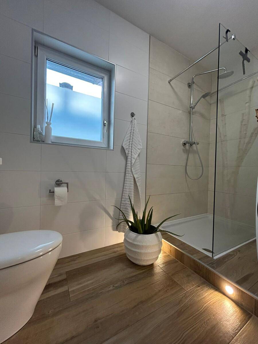 Modernes Badezimmer mit ebenerdiger Dusche, Wand-WC und Holzoptik-Fliesenboden.