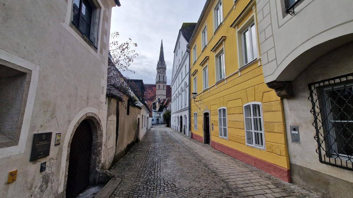 Enge Kopfsteinpflastergasse zwischen alten Gebäuden, die zu einem Kirchturm in der Ferne führt.