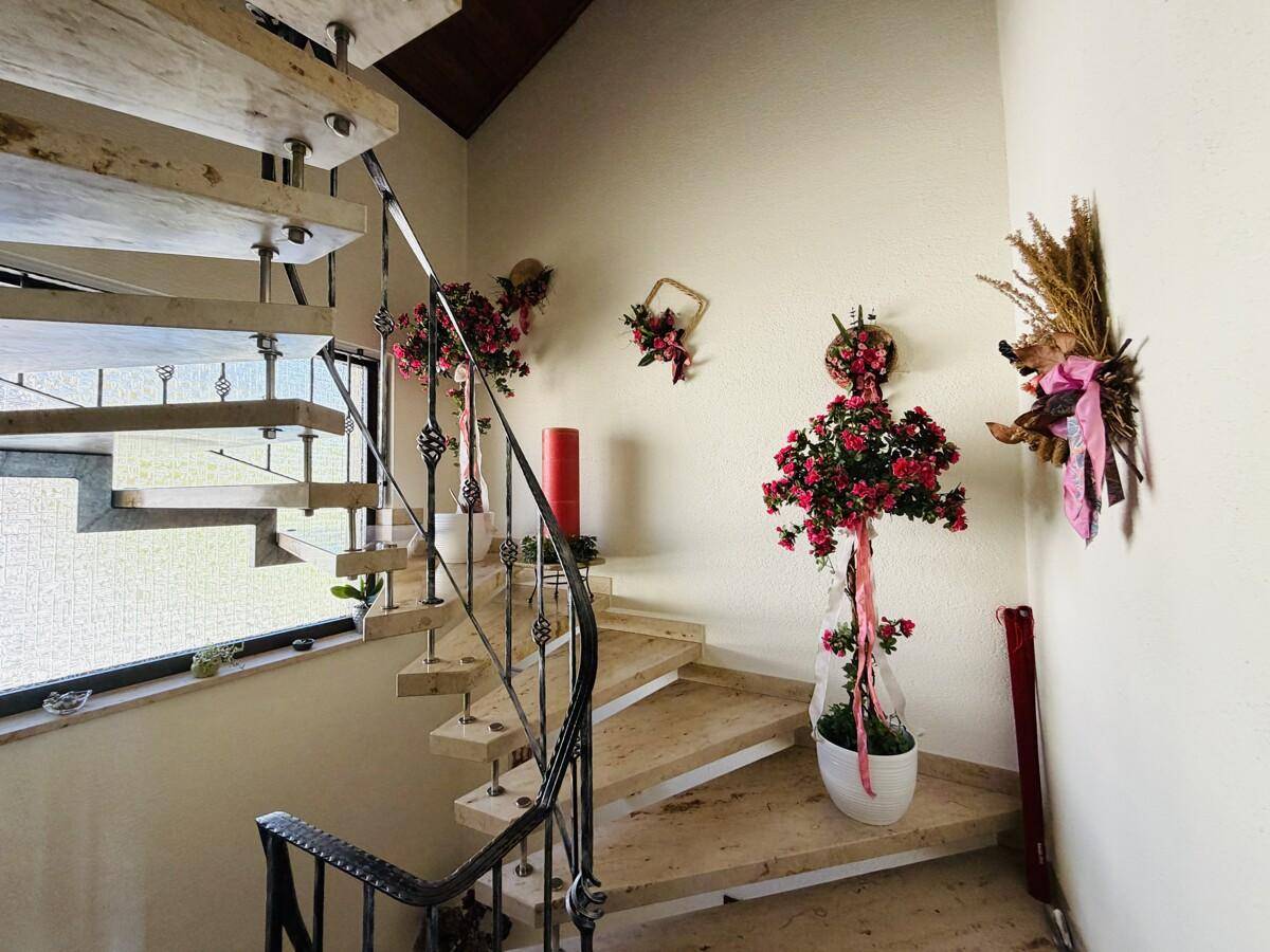 Heller Treppenaufgang mit geschwungener Metallbalustrade und dekorativen Blumenarrangements.