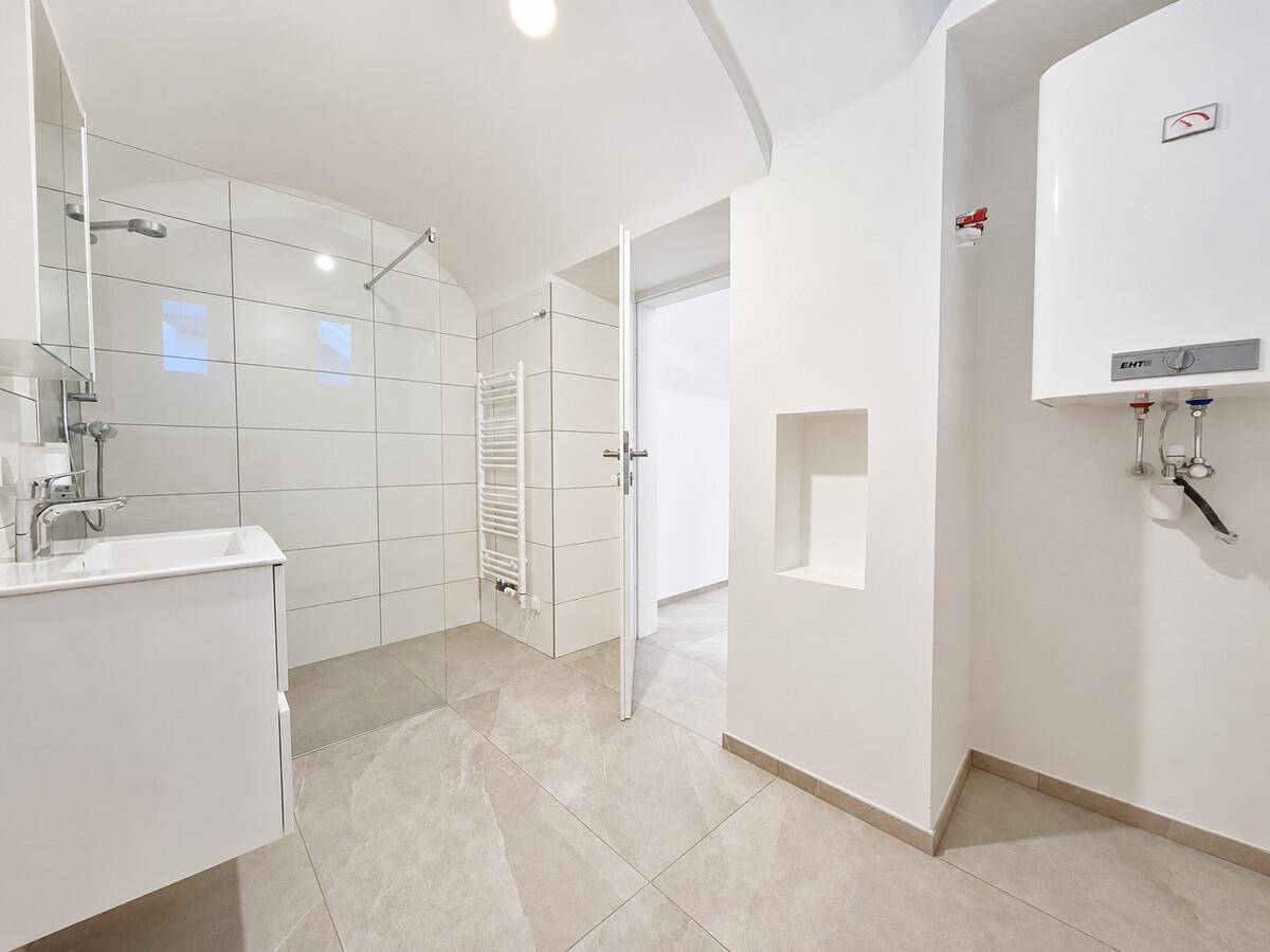 Funktionales Badezimmer mit Dusche, Waschtisch, beheiztem Handtuchhalter und Warmwasserbereiter.