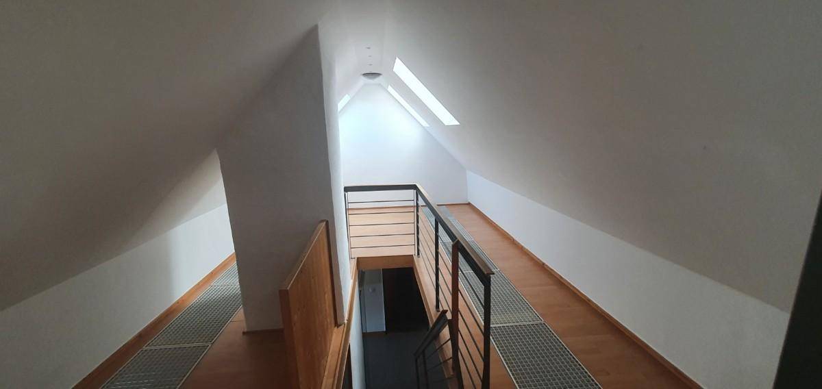 Heller Flur im Dachgeschoss mit Holzgeländer und Dachfenstern, die Licht spenden.
