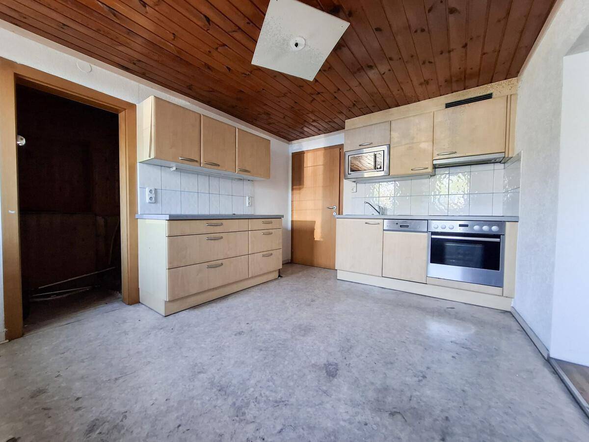Küche mit hellen Holzschränken, Einbaugeräten und einer Holzdecke.