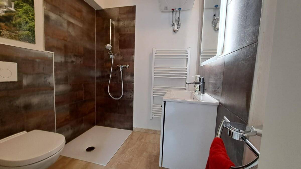 Modernes Badezimmer mit ebenerdiger Dusche, Wand-WC und beheiztem Handtuchhalter.