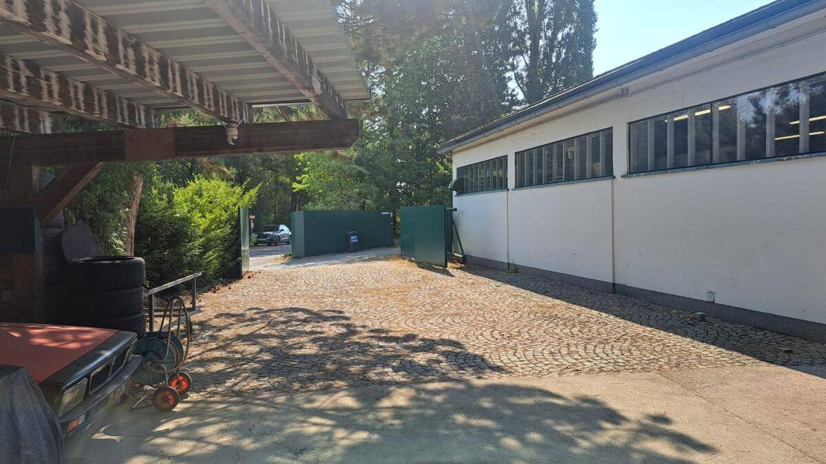Außenbereich mit gepflasterter Zufahrt, einem Carport und dem Eingang zum Werkstattgelände.