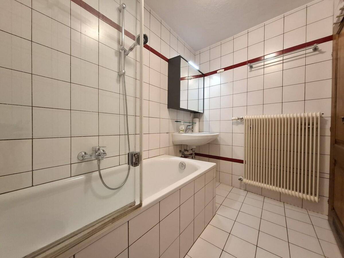 Gefliestes Badezimmer mit Badewanne, Duschvorrichtung und Heizkörper.