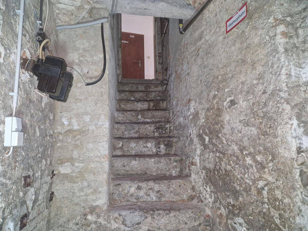 Steintreppe führt aus dem Kellerbereich nach oben, umgeben von rauen Wänden.