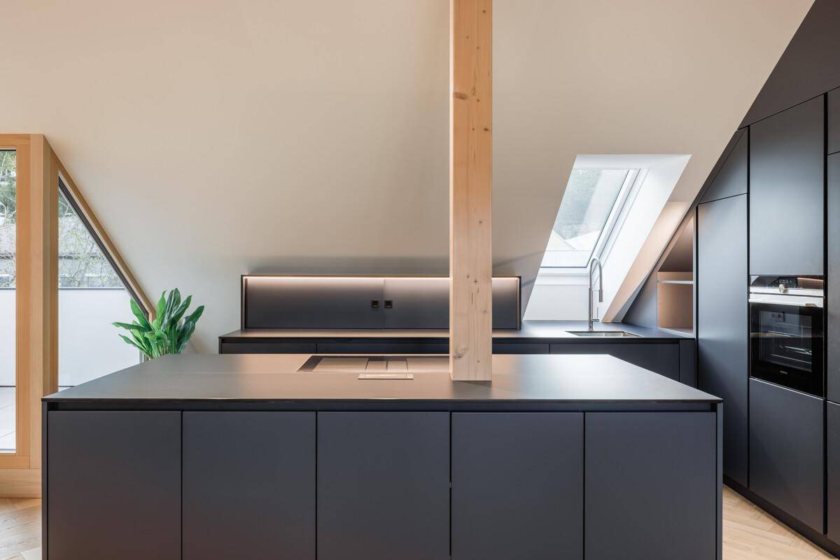 Moderne Küche im Dachgeschoss mit dunkler Kücheninsel, Holzbalken und Dachfenstern.