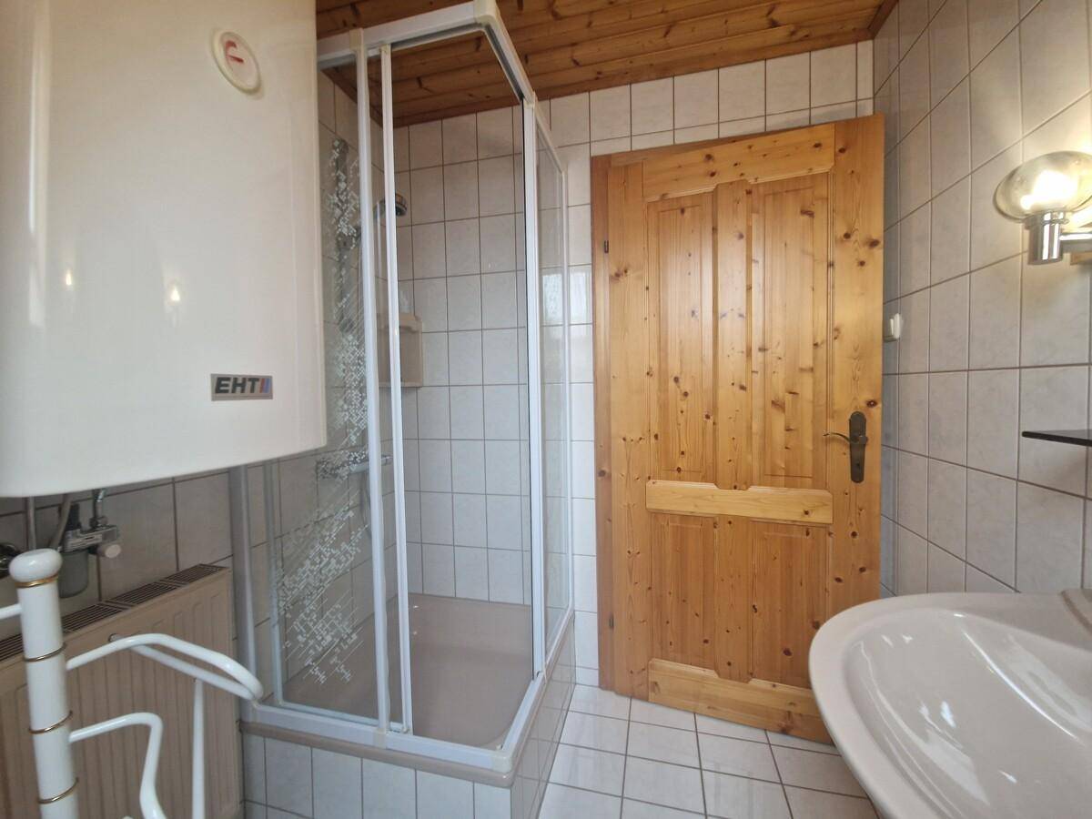 Kleines Badezimmer mit Duschkabine, Waschbecken und Holzdecke, hell gefliest.