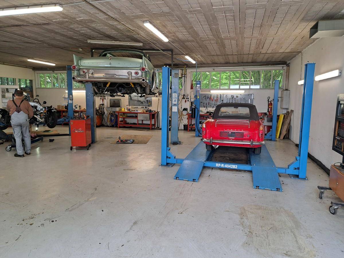 Helle Kfz-Werkstatt mit zwei Hebebühnen und Oldtimern, bereit für professionelle Wartungsarbeiten und Reparaturen.