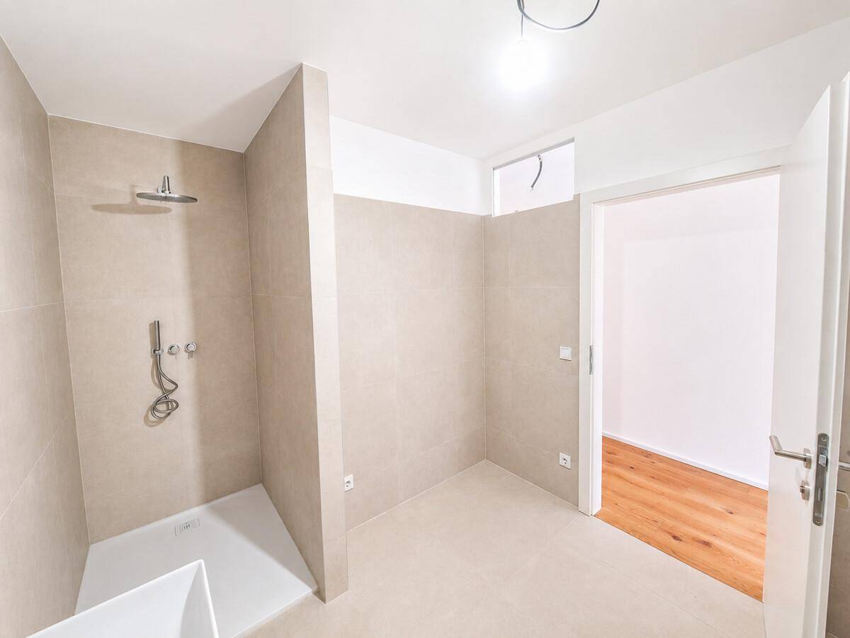 Helles Badezimmer mit begehbarer Dusche, beigefarbenen Fliesen und Zugang zu einem weiteren Raum.