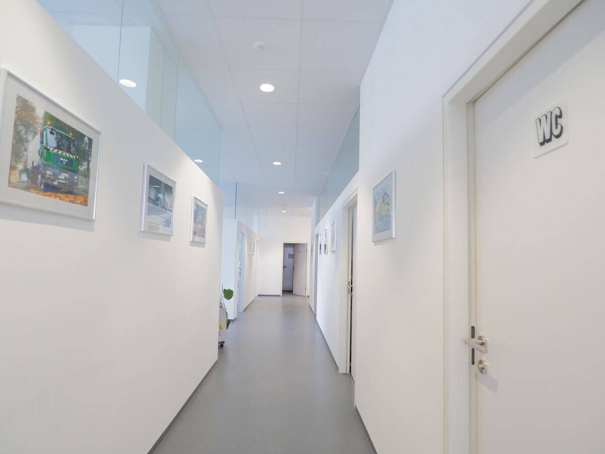 Langer, heller Flur mit weißen Wänden und Bildern, der zu verschiedenen Räumen führt.