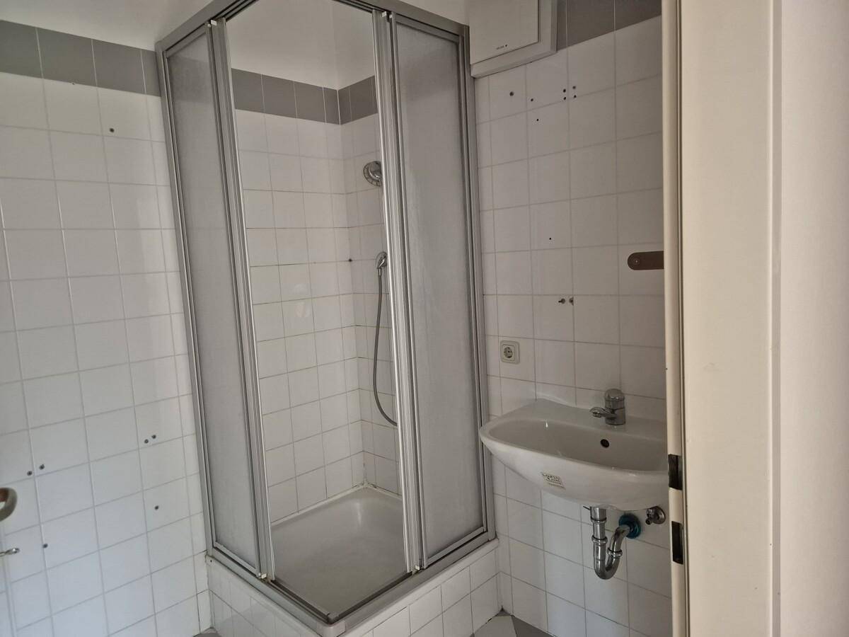 Badezimmer mit Duschkabine, Waschbecken und weißen Fliesen, akzentuiert durch eine graue Bordüre.