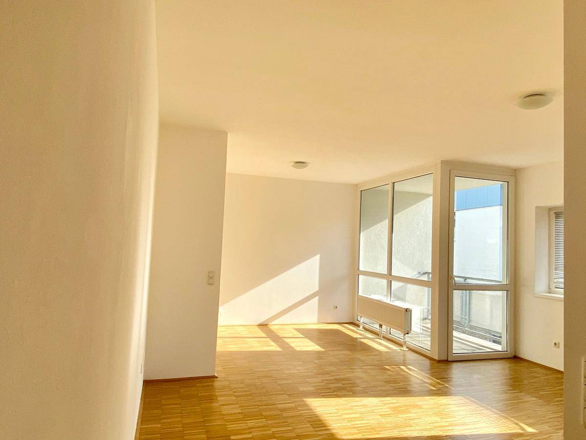 Lichtdurchfluteter Wohnbereich mit Parkettboden und großem Fenster zum Balkon.