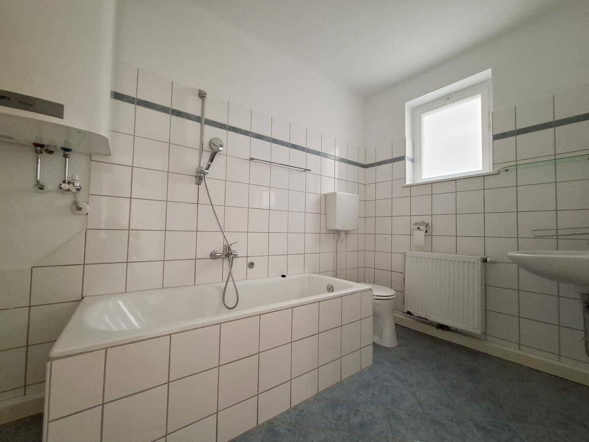 Badezimmer mit Badewanne, Dusche, WC, Waschbecken und Fenster, in gutem Zustand.