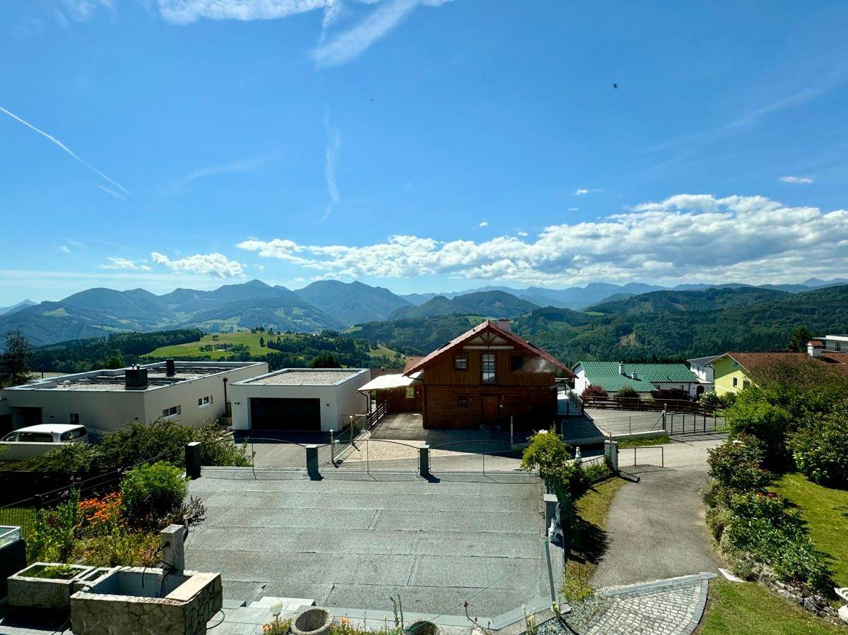 Weitläufiger Blick auf die Liegenschaft und die umliegende Berglandschaft unter blauem Himmel.