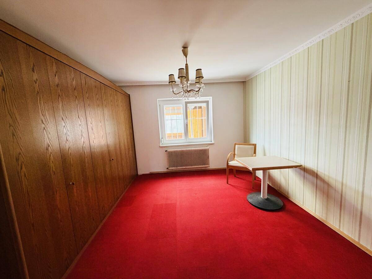 Schlafzimmer mit rotem Teppichboden, großem Einbauschrank und gestreifter Tapete.