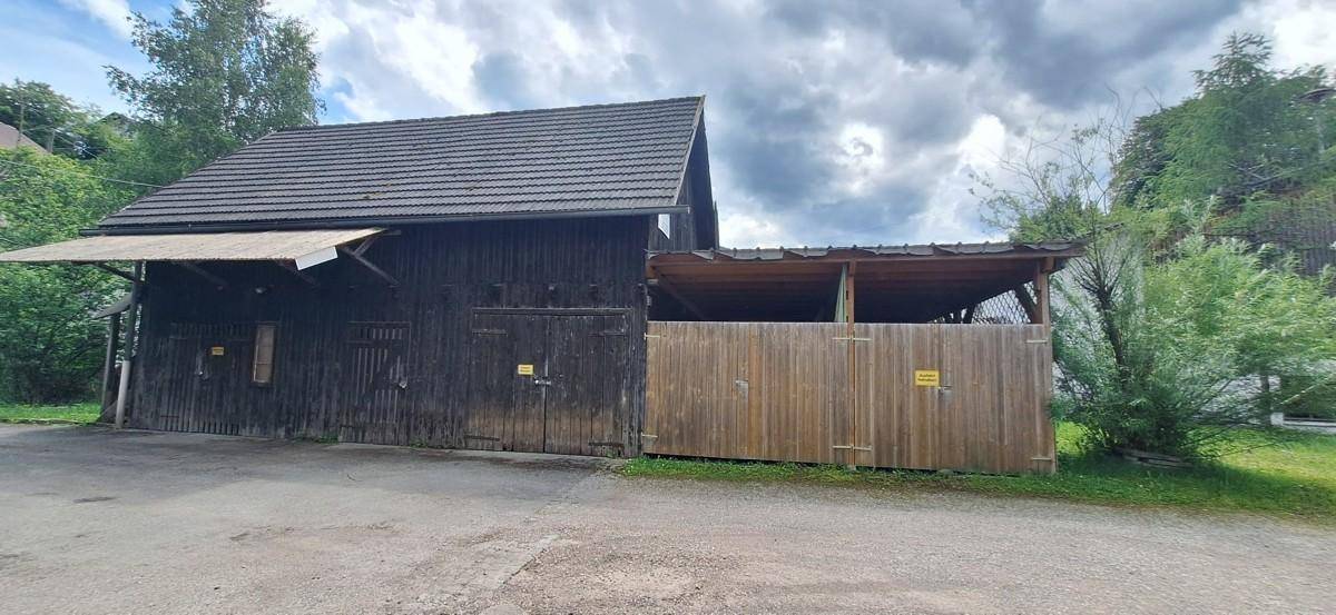 Rustikales Holzgebäude mit dunkler Fassade und einem überdachten Bereich, möglicherweise eine Scheune.