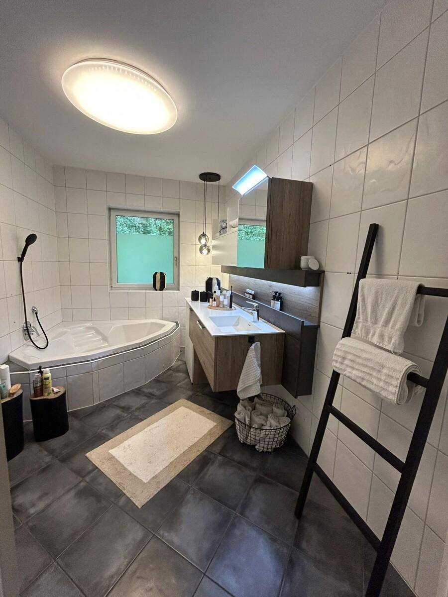 Helles Badezimmer mit modernem Waschtisch, Spiegelschrank und Eckbadewanne.
