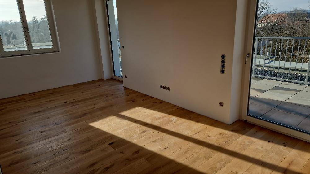 Heller Raum mit Holzboden und Zugang zu einem großen Balkon, ideal als Wohnzimmer.