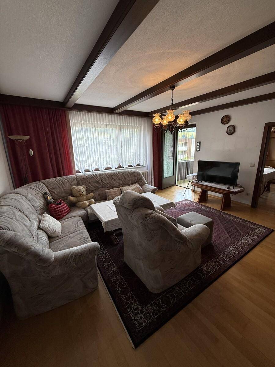 Traditionelles Wohnzimmer mit Holzbalkendecke, gemütlicher Sitzecke und Balkonzugang.