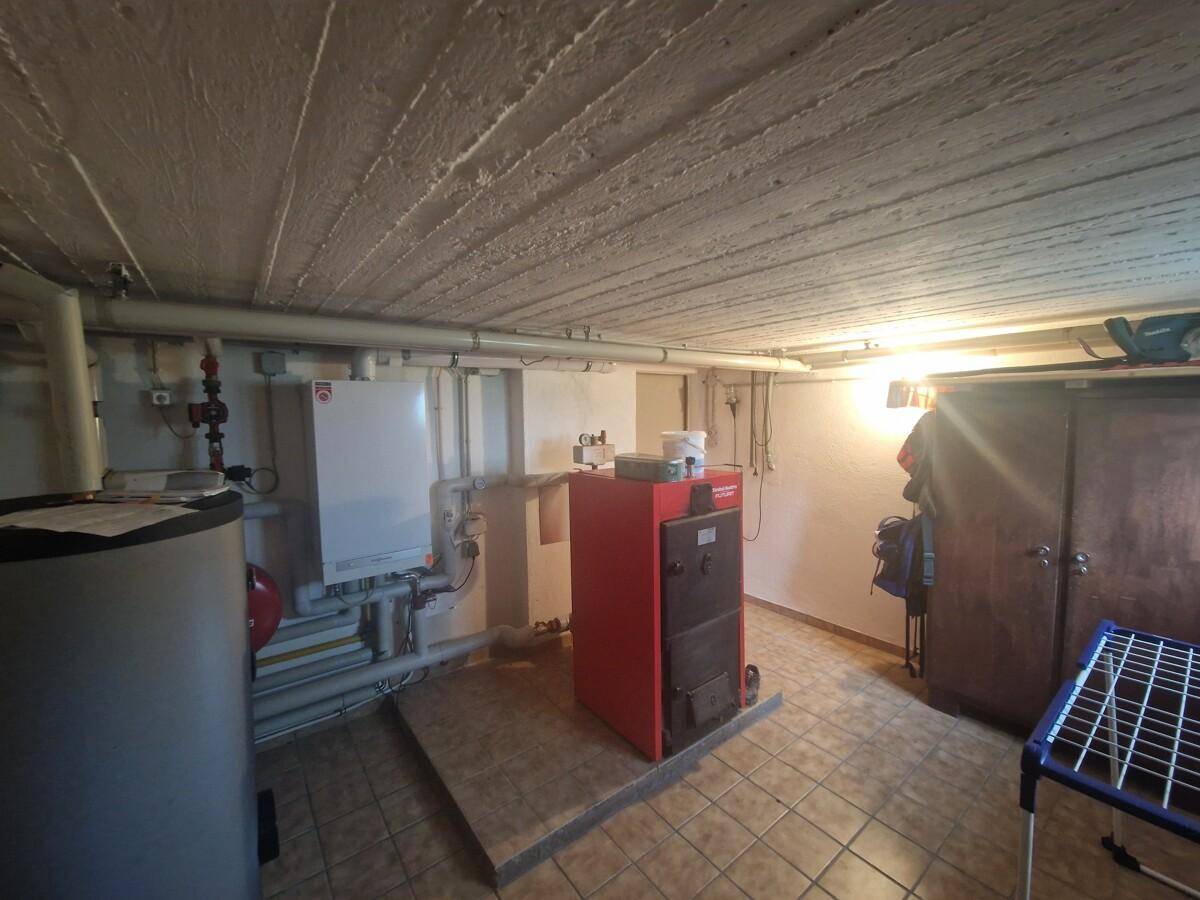 Heizungsraum im Keller mit Kessel, Warmwasserspeicher und Fliesenboden, funktional eingerichtet.