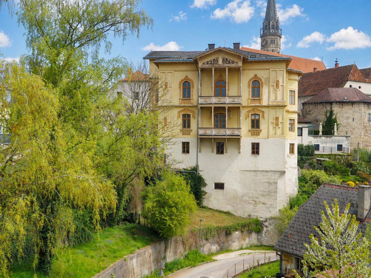 Historisches Gebäude in grüner Umgebung mit Blick auf die Stadt und Kirchturmspitze.