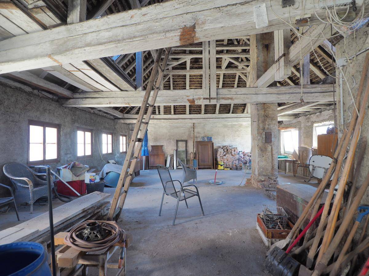 Geräumiger Dachboden mit freiliegenden Holzbalken und Fenstern, bereit für den Ausbau.