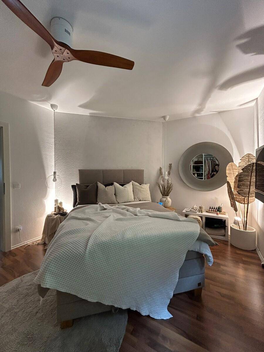 Schlafzimmer mit Doppelbett, Deckenventilator und warmem Laminatboden, modern eingerichtet.