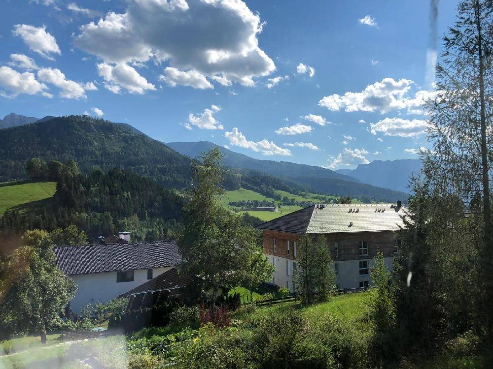 Häuser eingebettet in eine grüne Hügellandschaft mit weitem Blick auf die Berge unter blauem Himmel.