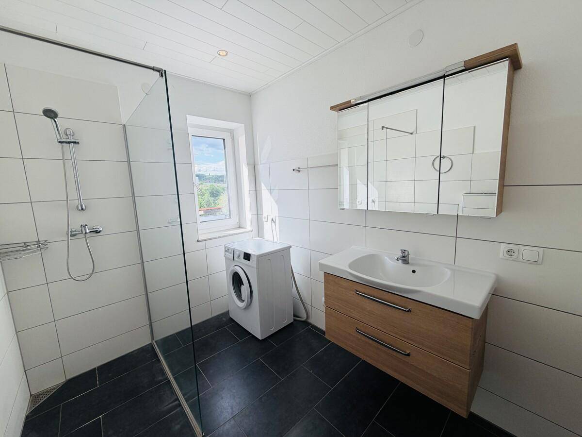 Helles Badezimmer mit großer Dusche, Waschbeckenunterschrank und Spiegelschrank.