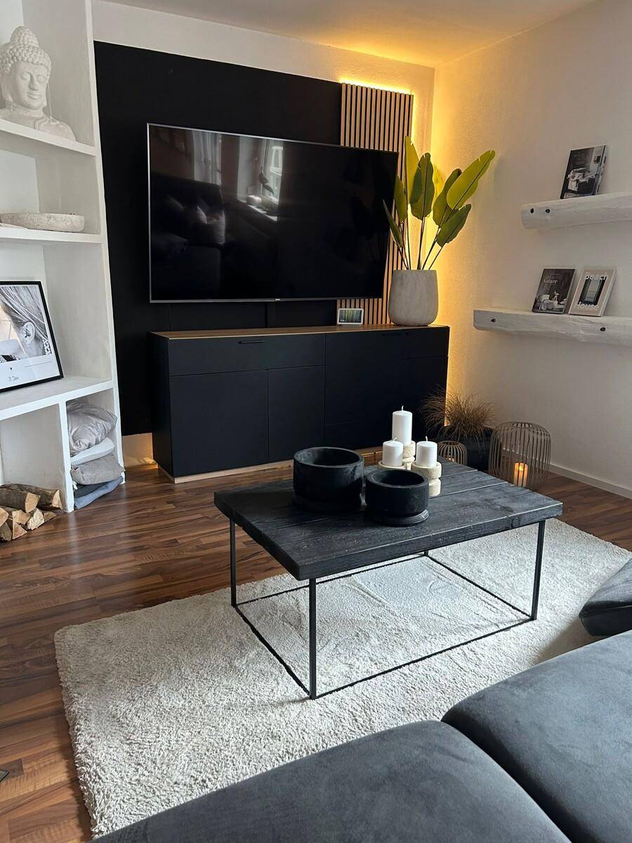 Modern eingerichtetes Wohnzimmer mit großem Fernseher, Couchtisch und dekorativen Elementen.